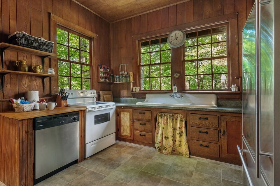 Prepare meals with a gorgeous WOODED VIEW and a winter LAKE VIEW.  Features old farmhouse sink, electric stove / oven, dishwasher, microwave (not shown, on rear wall) and refrigerator / freezer.