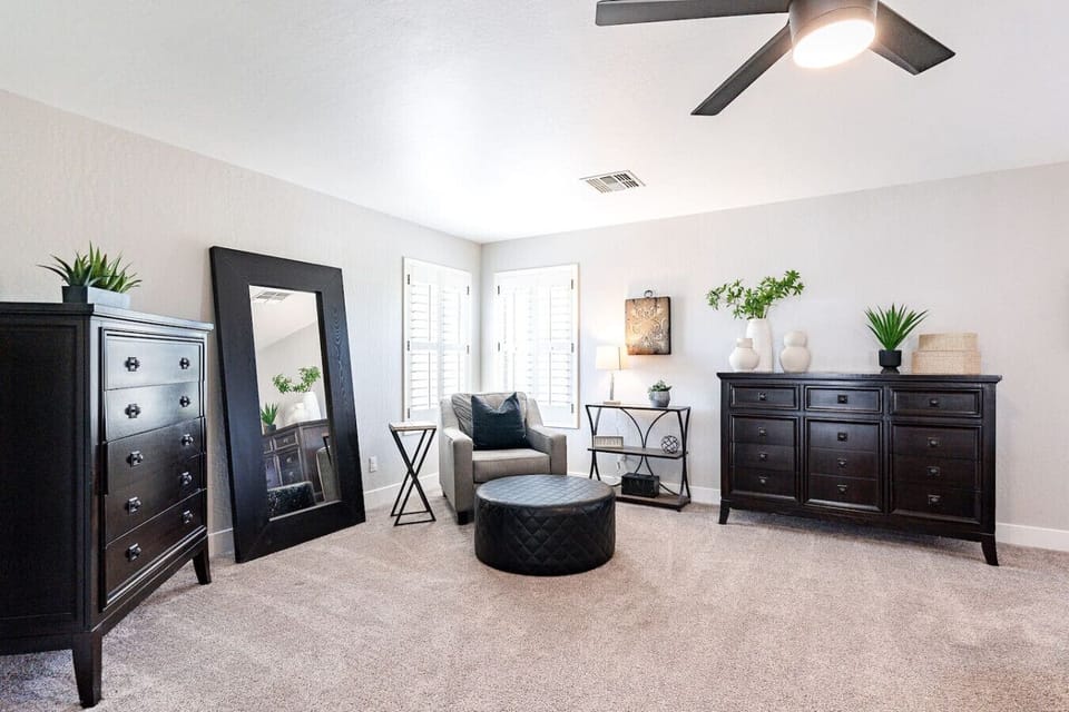 Elegant primary suite with king bed, dresser, seating corner, and full-length mirror.