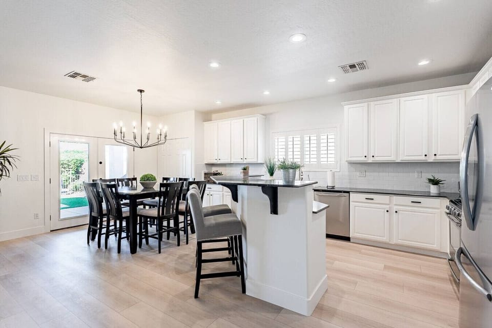 Modern open kitchen with breakfast bar seating and adjacent dining area with chandelier.