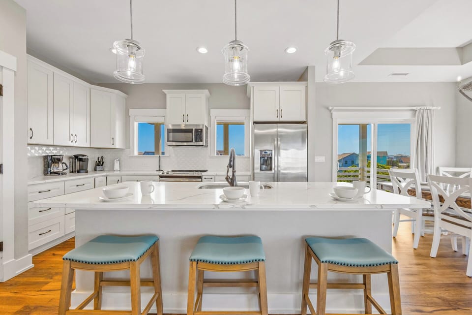 Gather around your bright kitchen island, where coastal-inspired stools and gleaming countertops set the stage for morning coffee and conversation with ocean views framing every moment.