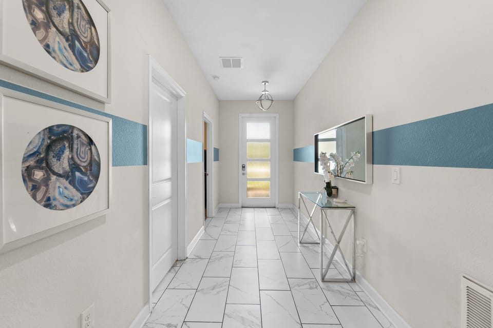 An elegant entrance hallway welcomes arrivals with its modern marble-look tile flooring, vaulted ceiling, and stylish blue accent walls, setting a refined and inviting tone for your stay.