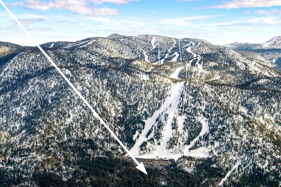 Aerial view reveals snow-covered ski slopes carving through forested mountains under bright winter skies.