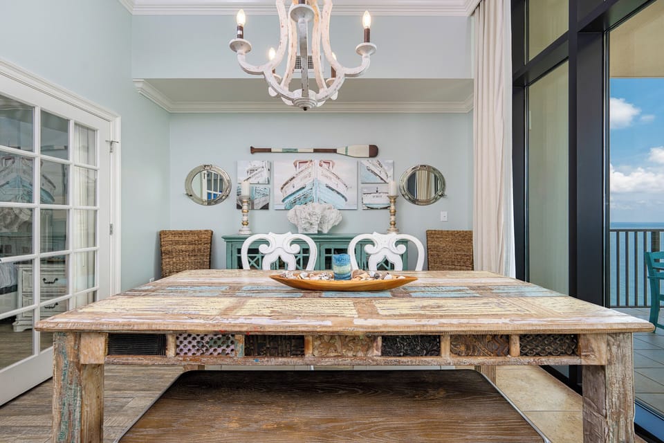 This dining area features a rustic wooden table, coastal decor, and a stunning beachfront view through large glass doors
