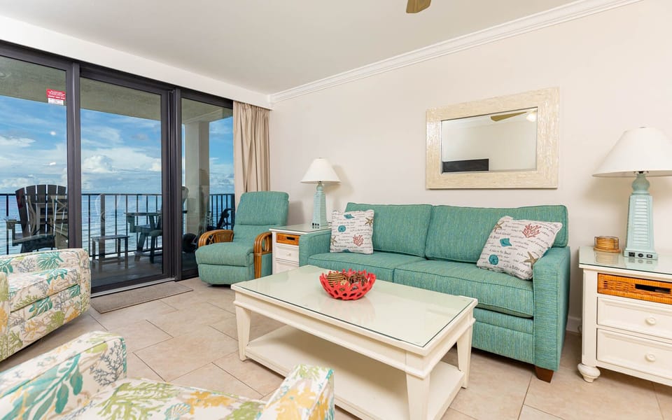 This living area features bright turquoise seating, a glass-top coffee table, and a breathtaking view of the beach