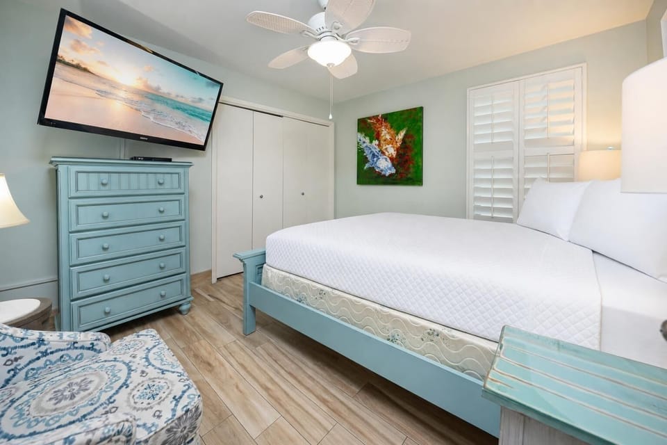 Guest bedroom featuring a cozy queen bed, stylish blue dresser, and a large TV for entertainment