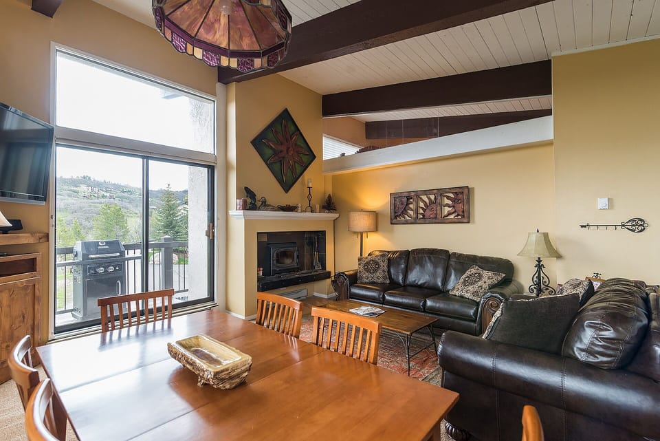Relax in your spacious open-plan living area featuring rich leather seating, rustic wood beams, and a cozy fireplace for mountain evenings.