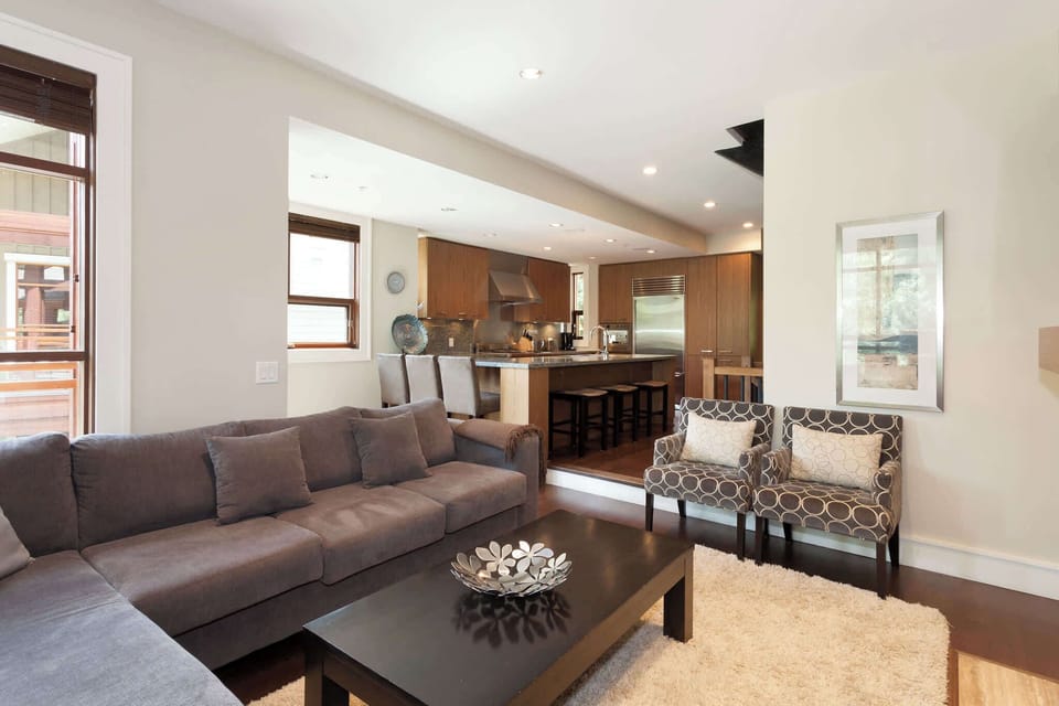 - Modern open-concept living room with plush sectional and warm neutral decor  
- Bright layout connects to the kitchen for relaxed gatherings or movie nights  
- Floor-to-ceiling windows bring in natural light and mountain lodge charm  