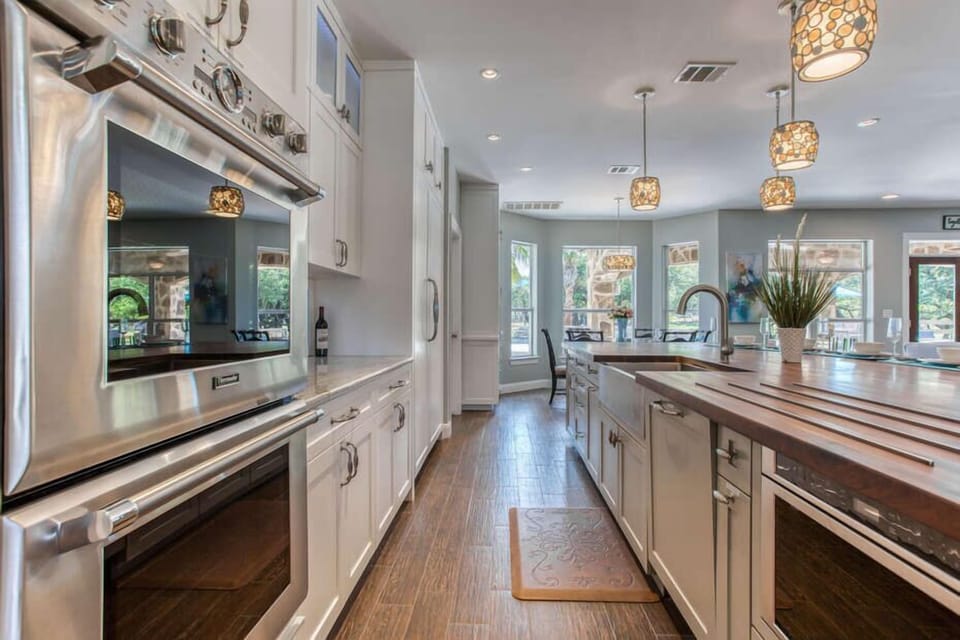 All New and Fully Equipped Chef's Kitchen with Stainless Steel Appliances Including Double Ovens, Large Refrigerator, and Plenty of Windows with Views of the Backyard