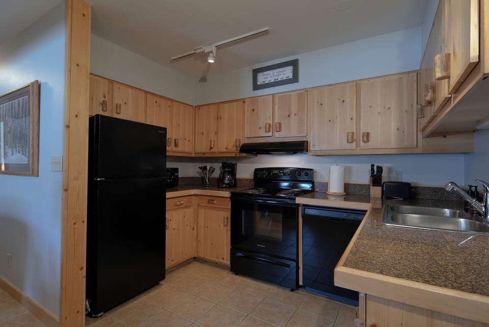 Your fully equipped kitchen awaits with warm wood cabinets and modern appliances—imagine preparing your favorite meals while mountain views peek through the window, making every cooking moment feel like a cozy retreat.