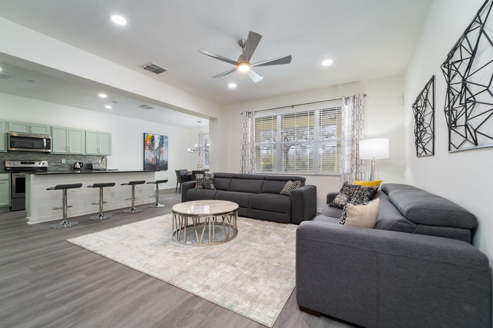 Open concept living rom with gray sofas, round coffee table, area rug, ceiling fan, recessed lighting, and breakfast bar seating connecting to the kitchen.