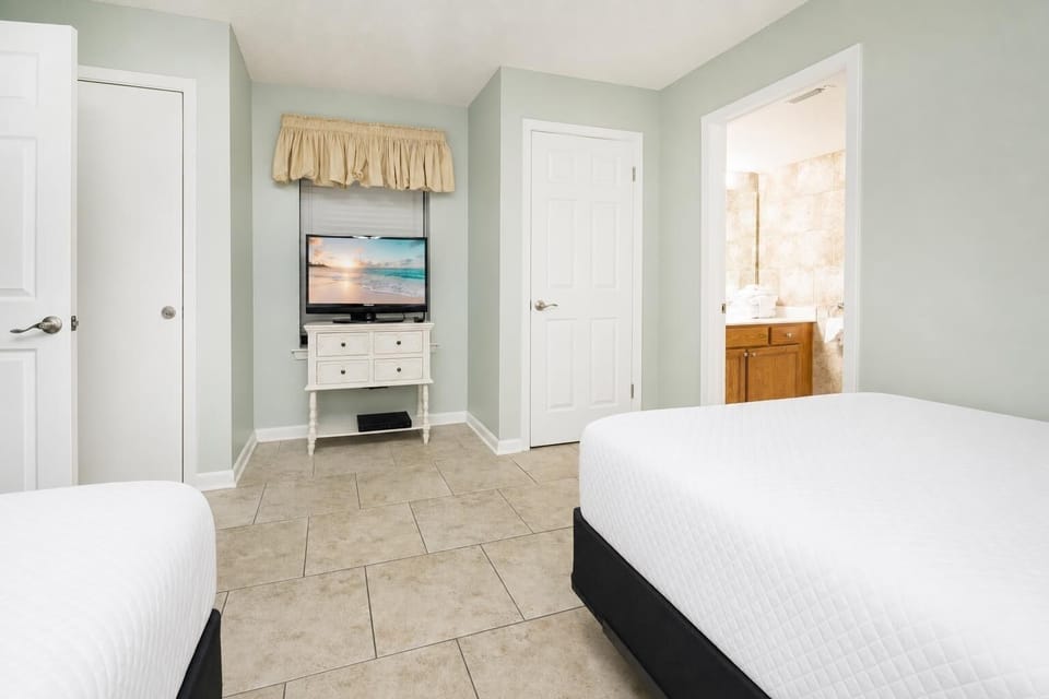 Inviting guest room featuring two beds, a queen and a double, a TV, and easy access to the adjoining guest bath