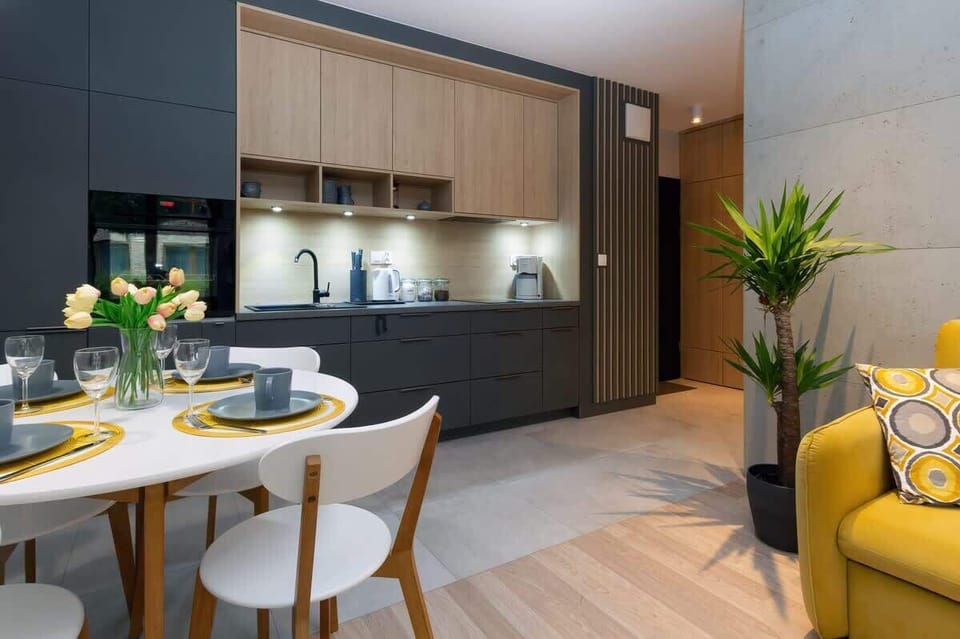 A contemporary dining space with a sleek wooden table and gray cushioned chairs. There is a decorative pendant light above the table, and the area is integrated into an open-plan kitchen.