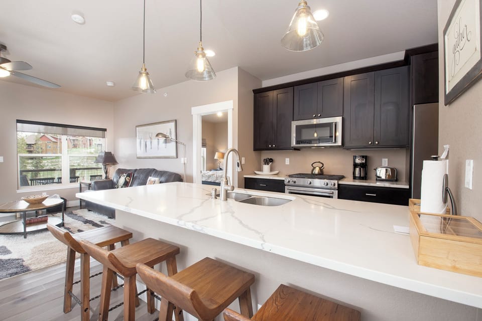 Your modern kitchen features gleaming quartz counters, sleek dark cabinets, and a breakfast bar perfect for morning coffee or evening conversations.