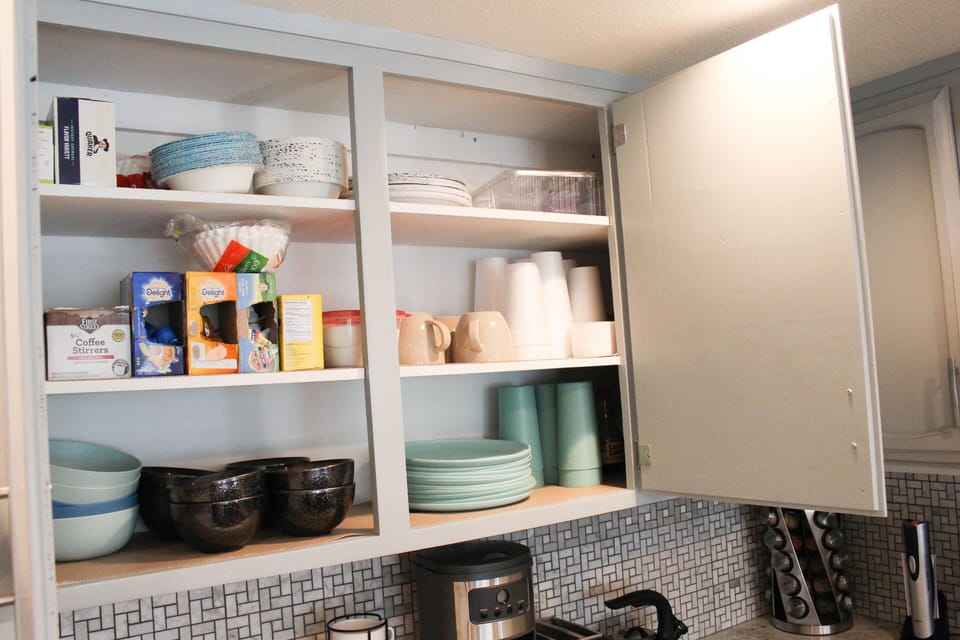 Our Kitchen is stocked with plates, cups, coffee, and pots and pans.