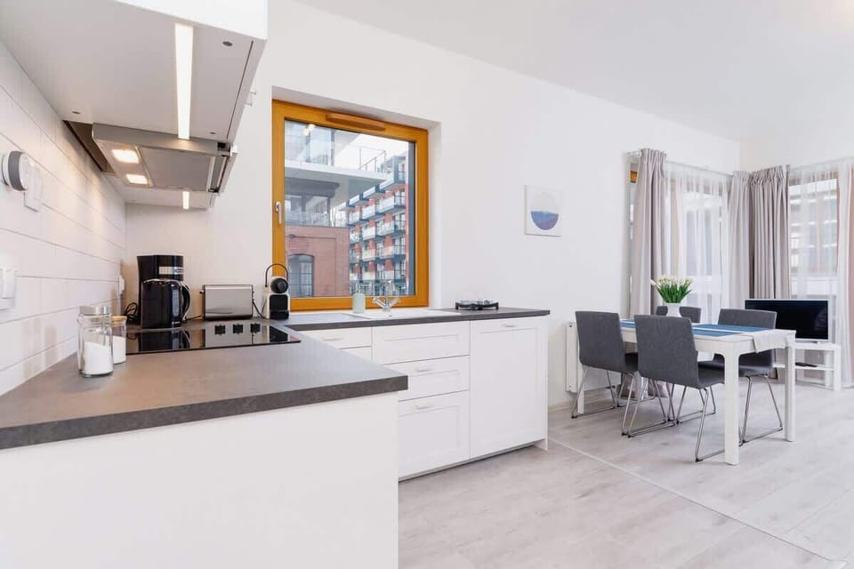 A combined kitchen and living space with an open layout. It features modern furnishings, including white cabinets and a dining table.