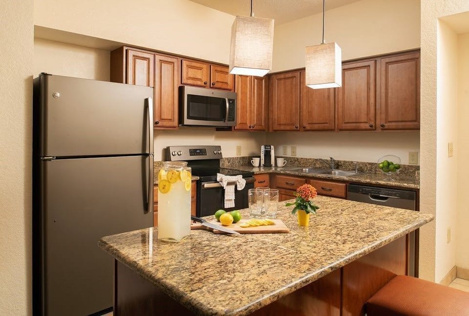 Full kitchen with wooden cabinetry, stainless steel fridge and oven, granite countertops, and two bar stools