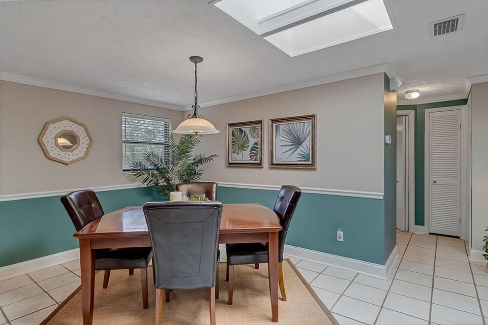 - Gather for meals in this cozy dining nook under a glowing skylight and soft pendant light
- Four leather chairs surround a polished wooden table for shared laughs and dining
- Tropical prints and calming hues set the tone for peaceful mealtimes