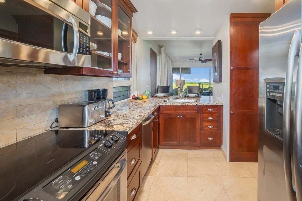 A modern kitchen with stainless steel appliances, granite countertops, and rich wooden cabinetry, offering a bright open view into the living area and outdoors.