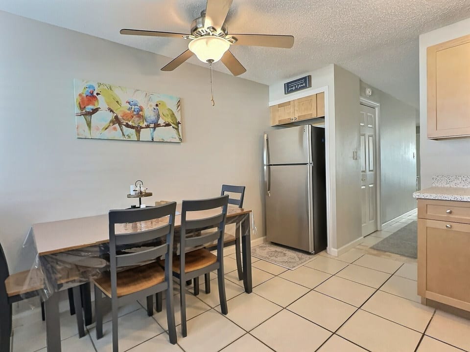 Open dining area with table, chairs, ceiling fan, and stainless refrigerator