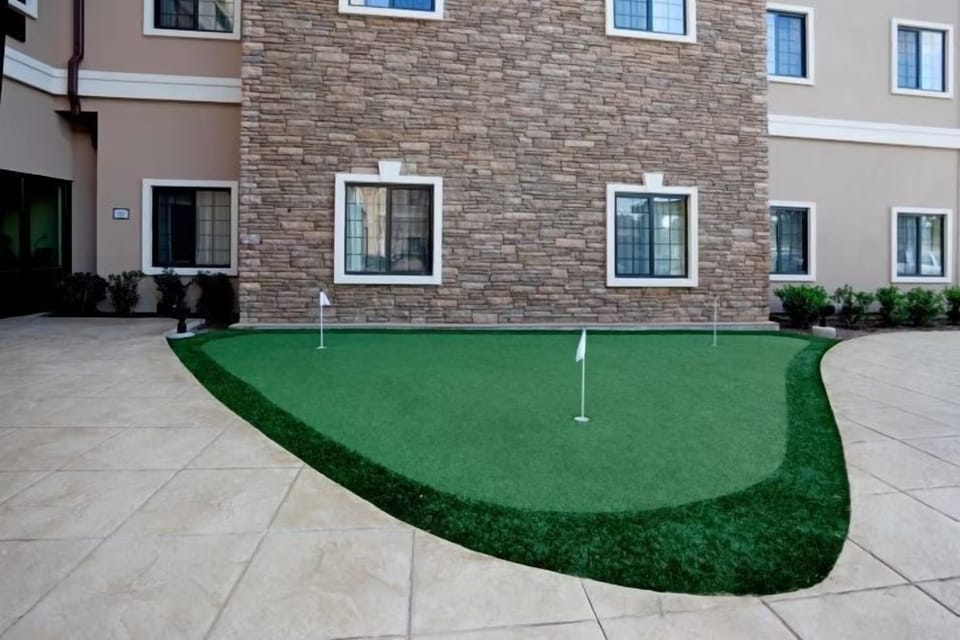 Putting green on vibrant turf, bordered by stone walls and sunny windows