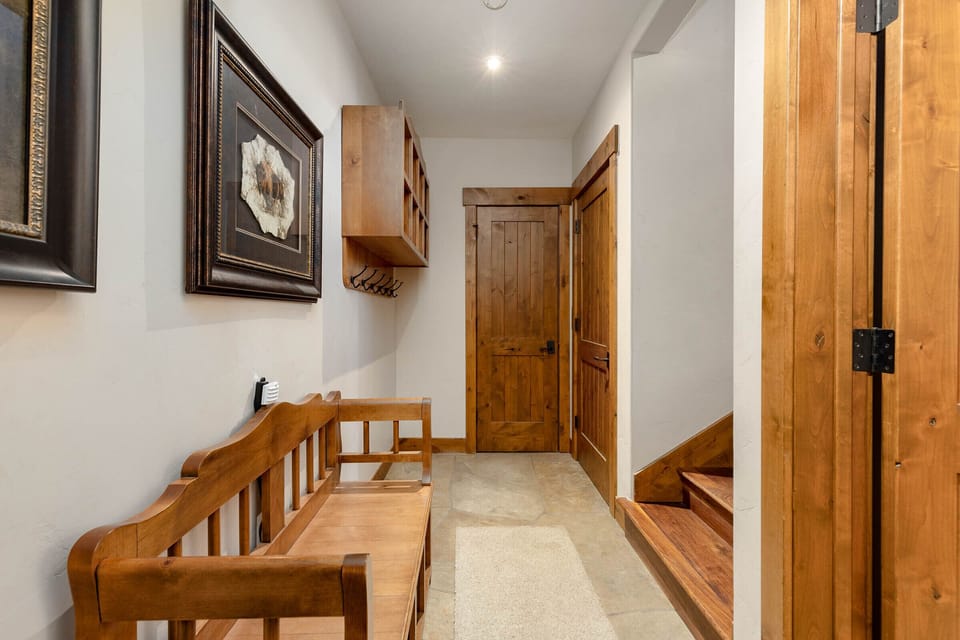 Hallway entrance from garage, with wooden bench, framed artwork on wall, wooden cabinets, coat hooks, and a closet.