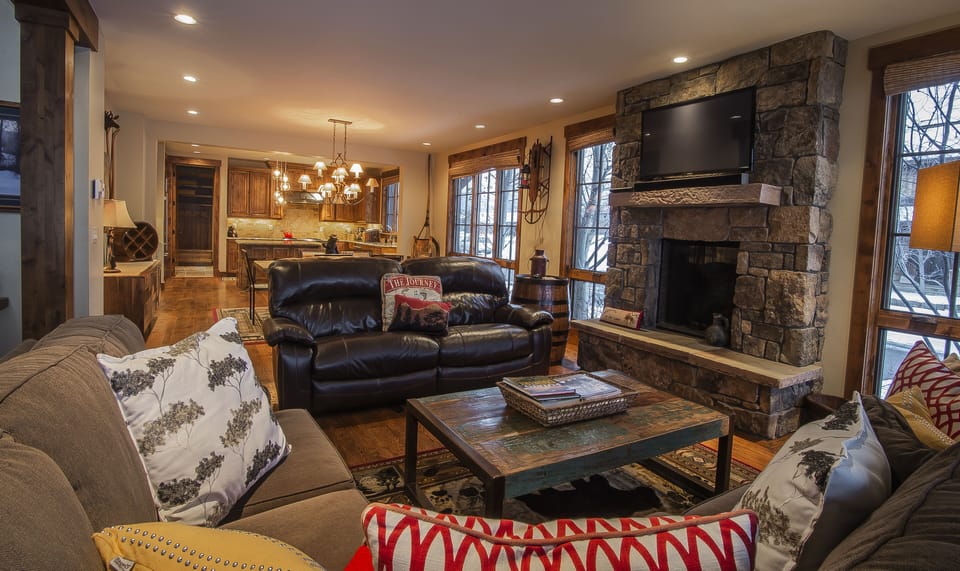 Cozy up in your mountain retreat's living room where rustic stone fireplace warmth meets modern comfort. Sink into plush sofas while you watch your favorite shows or gaze out at winter views through large windows.