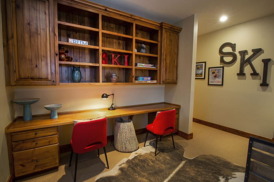 Your perfect mountain retreat workspace awaits! Settle into this cozy ski lodge office with rich wood built-ins, vibrant red chairs, and that unmistakable alpine charm.