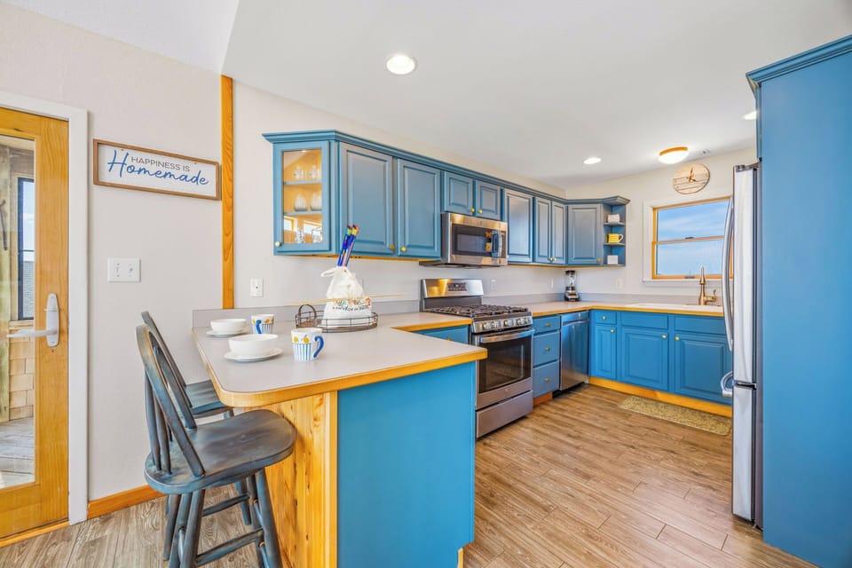 Your fully equipped kitchen features cheerful blue cabinetry, stainless steel appliances, and a cozy breakfast bar—perfect for preparing meals and gathering over morning coffee.