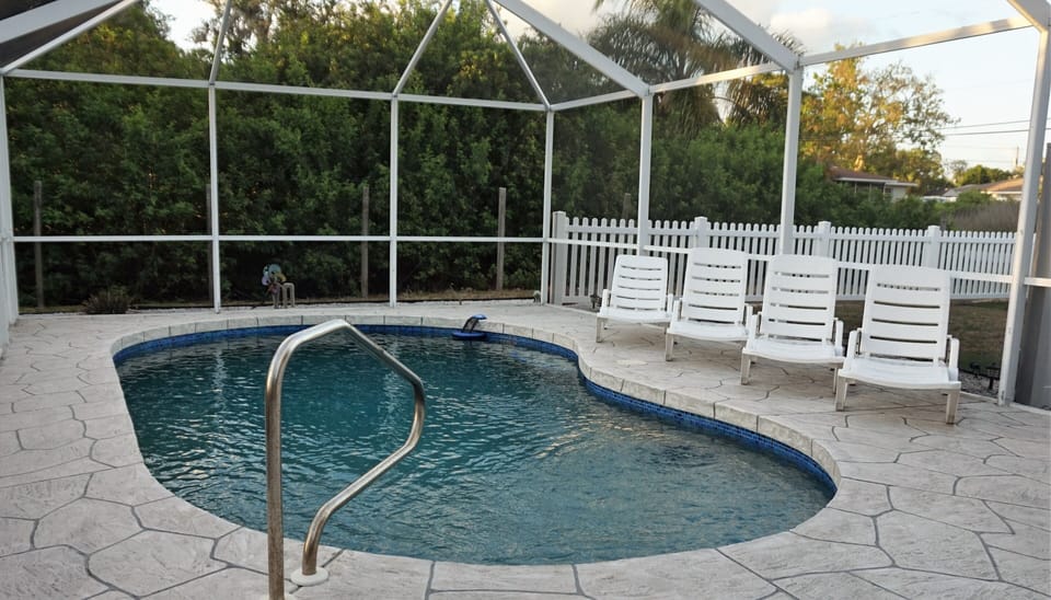 Screened in pool area with pool loungers and chairs. 