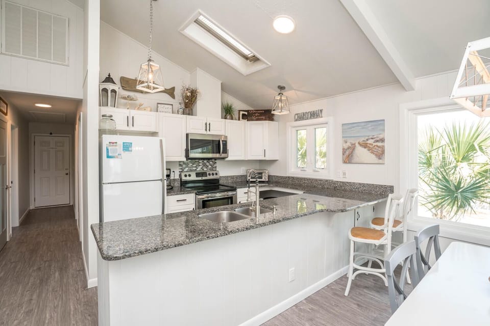 Light-filled coastal kitchen featuring granite countertops, white cabinetry, stainless steel appliances, skylight, and a spacious breakfast bar—ideal for cooking, casual dining, and gathering with family and friends.