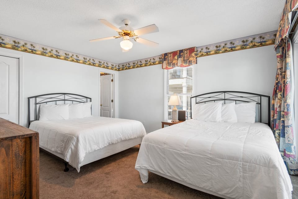 Unwind in your spacious bedroom with two comfortable beds, crisp linens, and gentle ceiling fan creating the perfect retreat.