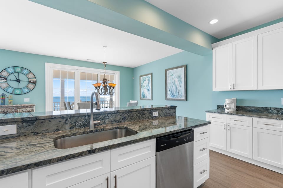 Your coastal kitchen features stunning marble countertops and gleaming white cabinets, with ocean views through the French doors.