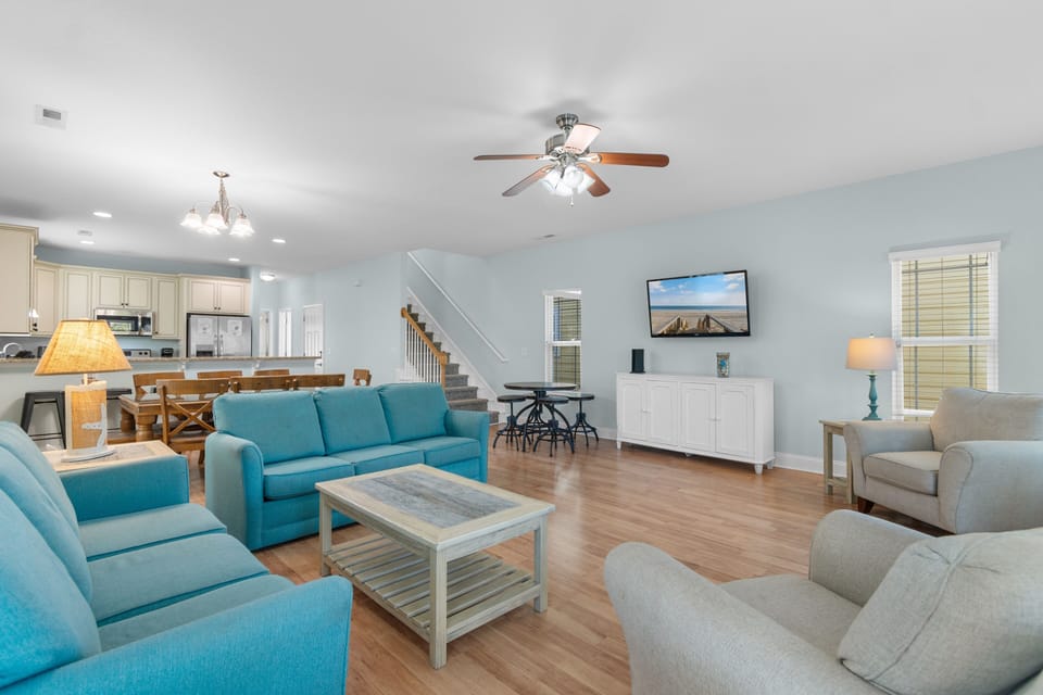 Relax in your spacious living room with vibrant turquoise seating and warm wood floors, perfectly positioned near the open kitchen.