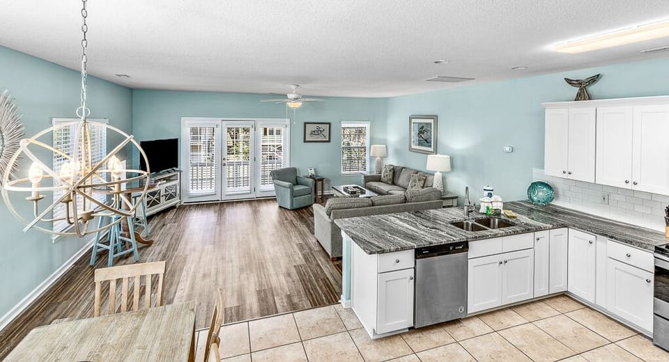Your open-concept coastal retreat combines kitchen, dining, and living spaces with soothing blue walls and modern amenities for comfortable gatherings.