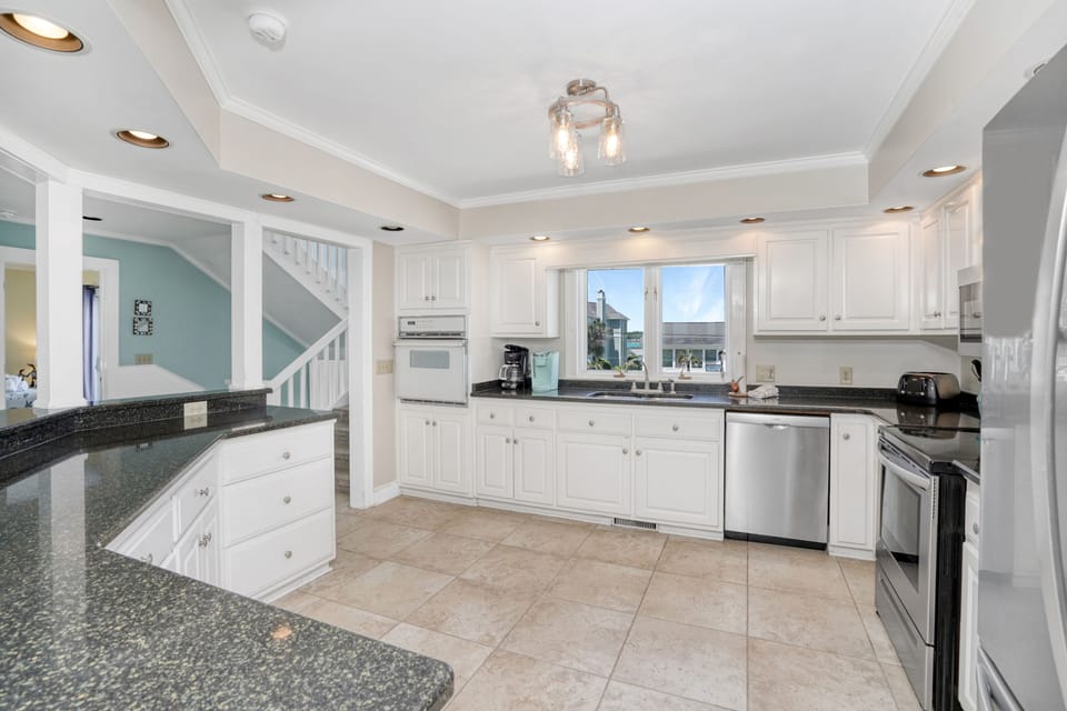 Your spacious kitchen features elegant white cabinetry, granite countertops, and stainless steel appliances, perfect for preparing meals with ocean views.