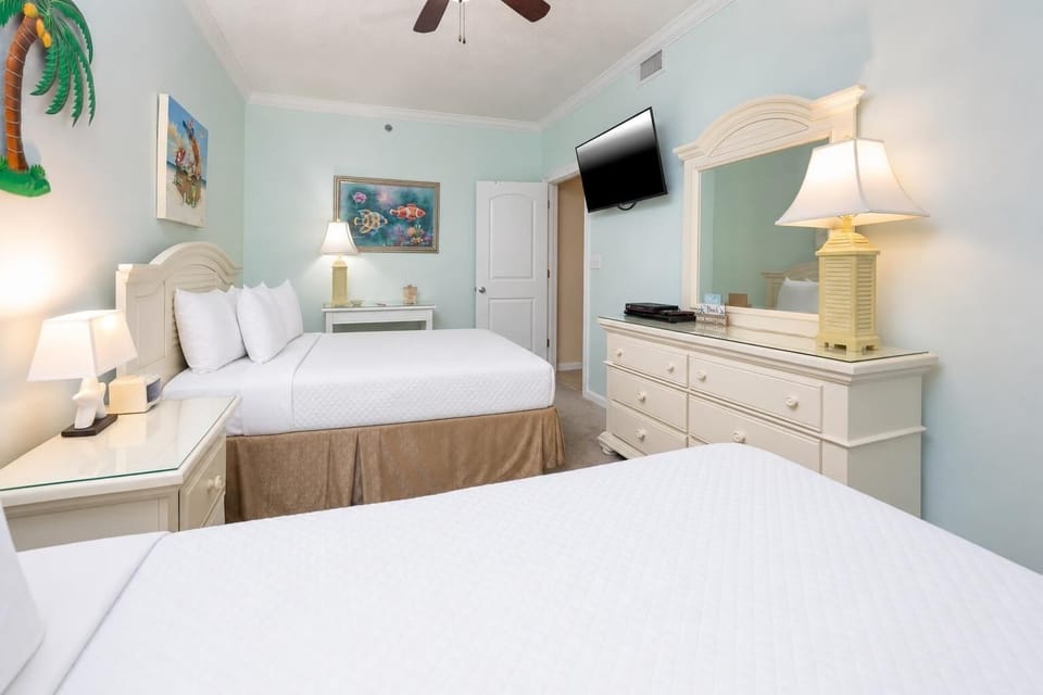 Bright guest bedroom featuring two double beds, a wall-mounted TV, and coastal artwork, creating a cheerful atmosphere