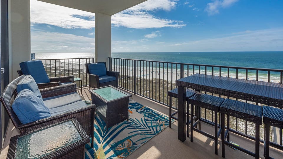 Cozy balcony features comfortable seating and a high-top table, offering sweeping views of the tranquil gulf and beach below