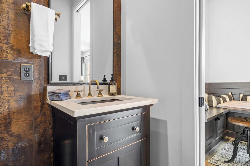 Modern bathroom featuring a sleek vanity, elegant gold fixtures, geometric mirror, and a walk-in glass shower with stylish tilework.
