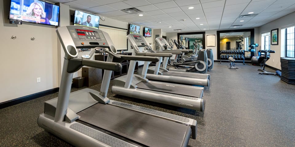 Fitness center with treadmills, dumbbells, and wall-mounted TVs