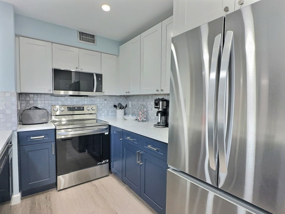 Kitchen with navy lower cabinets, stainless refrigerator, and stone countertops