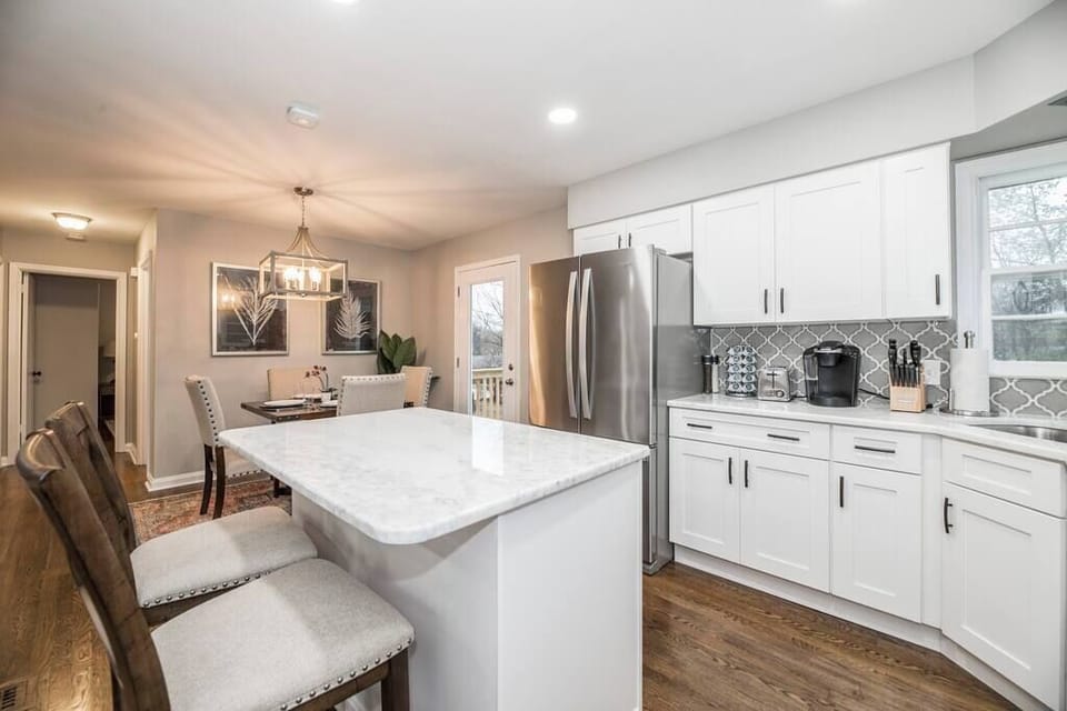 Bright, white-inspired kitchen featuring a center island with two chairs, luxurious cabinets, and modern appliances.