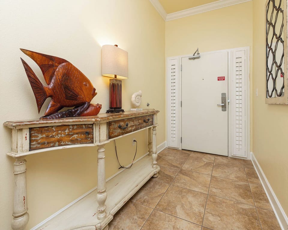 A welcoming entryway features a charming wooden fish sculpture, warm lighting, and a rustic console table
