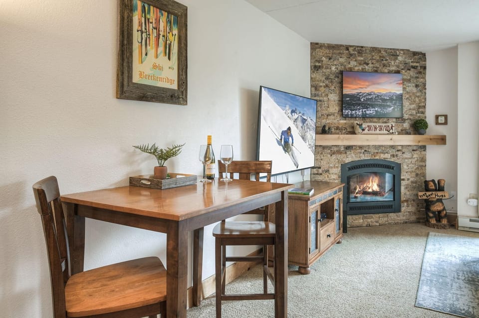 Wood dining table with two chairs sits beside a stone fireplace and flat-screen TV in the living area.