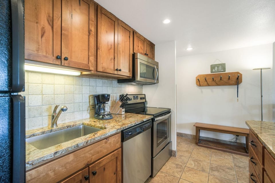 Granite countertops and stainless steel appliances line the kitchen, with natural wood cabinets overhead.