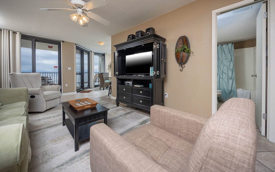 Living area features a comfortable green sofa, a cozy armchair, and a TV cabinet, with access to a balcony