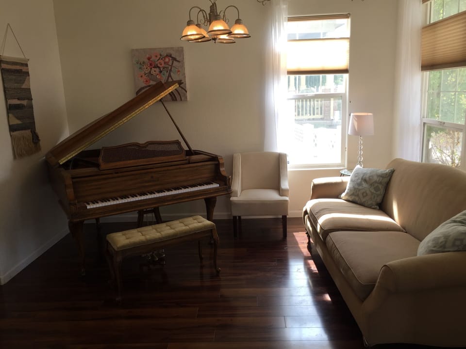 Sunlit sitting room with baby grand piano and elegant cozy seating