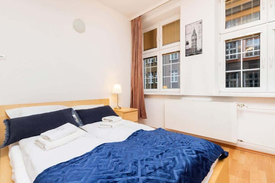 A cozy bedroom featuring a large bed with dark blue bedding, natural light streaming in through a large window, and wooden beams adding a rustic touch.