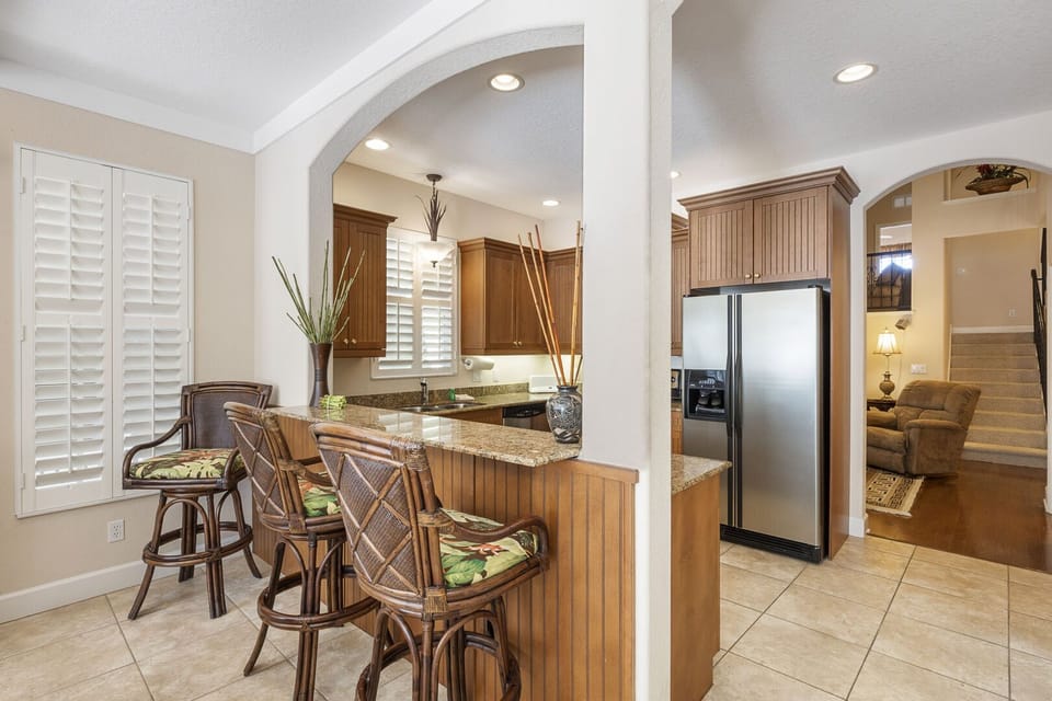 Open kitchen and dining area with bar seating, stainless refrigerator, and wicker furniture in background