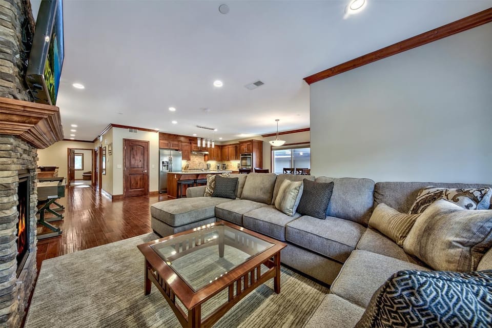Relax in your spacious living room featuring plush sectional seating, stone fireplace, and open-concept kitchen perfect for entertaining.
