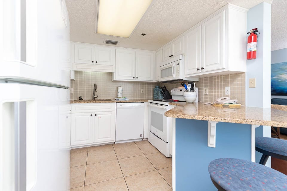 Prepare meals at the granite countertop, surrounded by bright cabinetry and white appliances